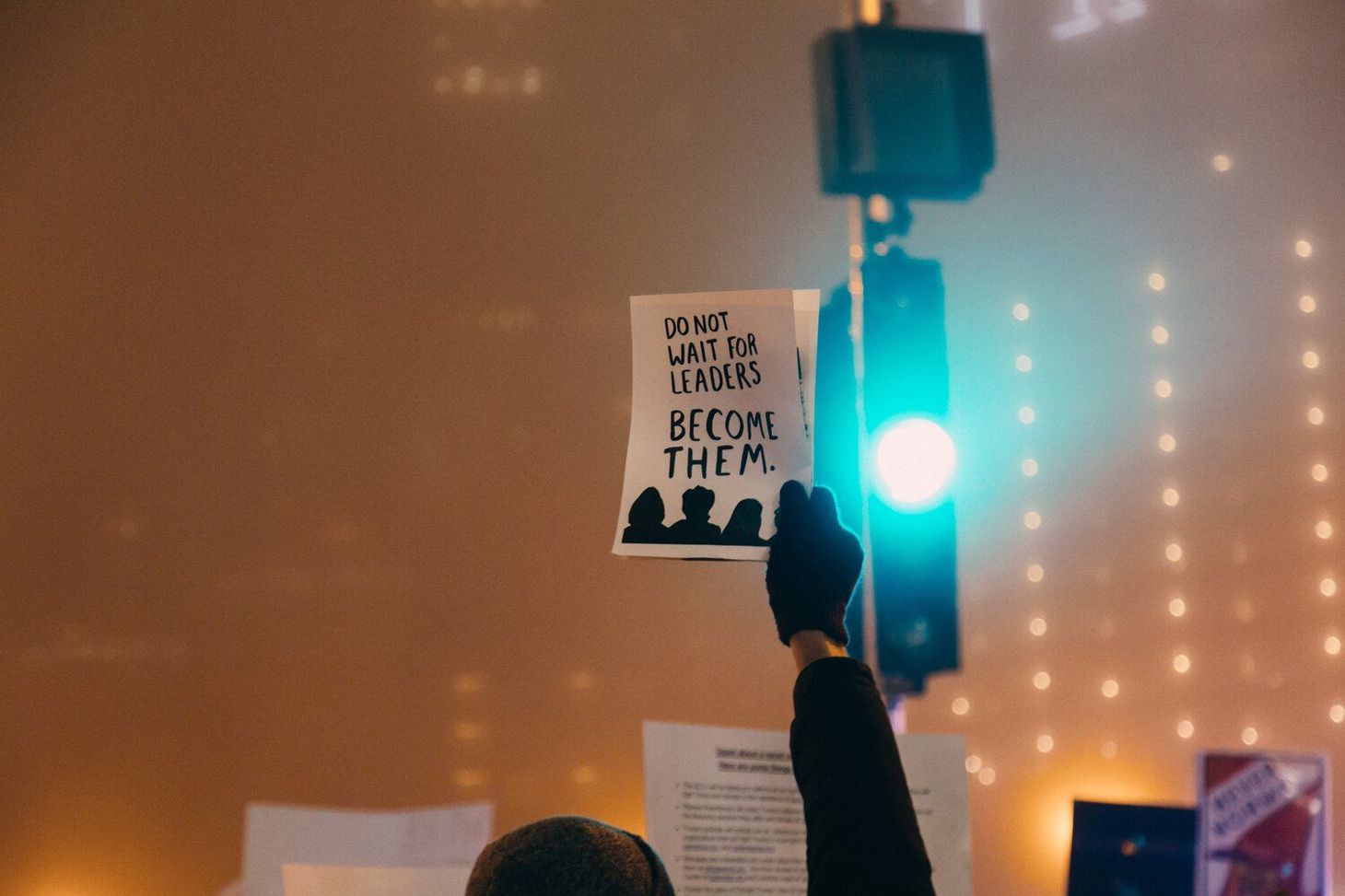 hand holding sign saying "Do not wait for leaders. Become them."