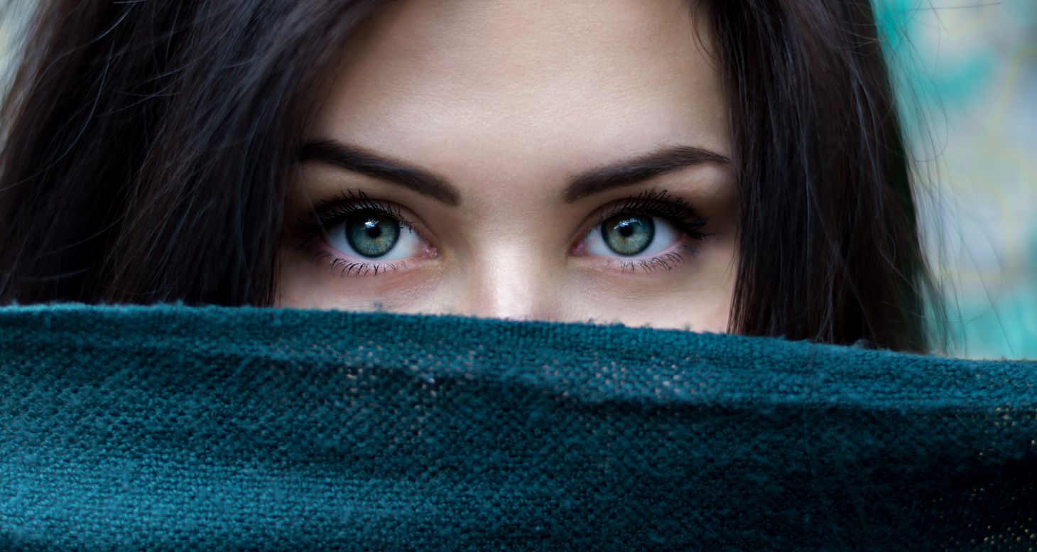 a dark haired white woman with green eyes and dark eyebrows looks towards the camera. her mouth is obscured
