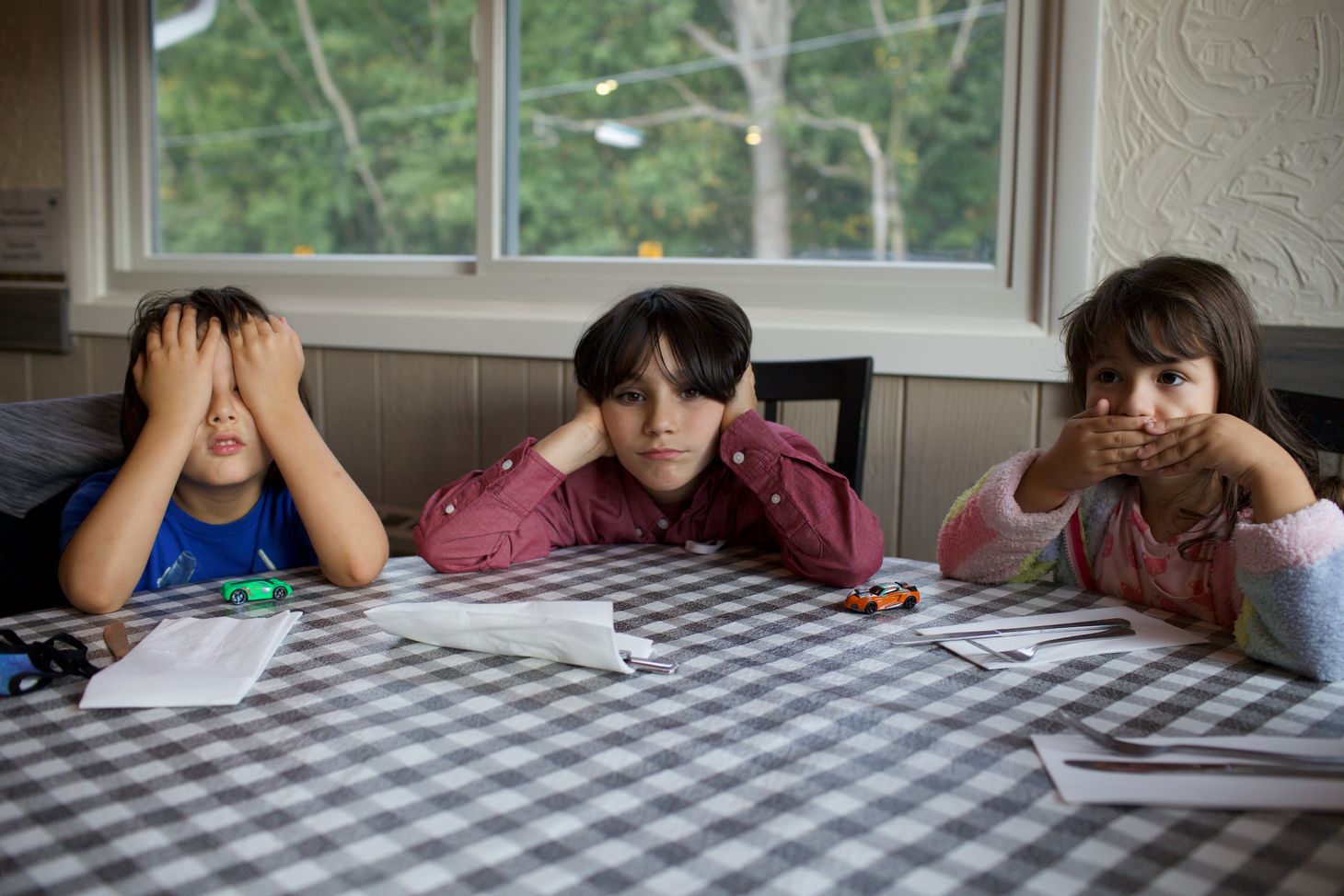 three children sitting at a table - one covering their eyes, another their ears, and the third, their mouth