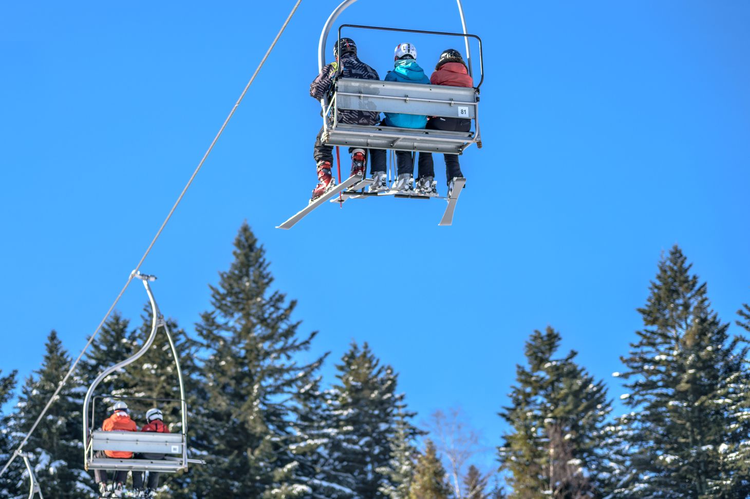 Skiers sitting on a chair lift against a bright blue sky